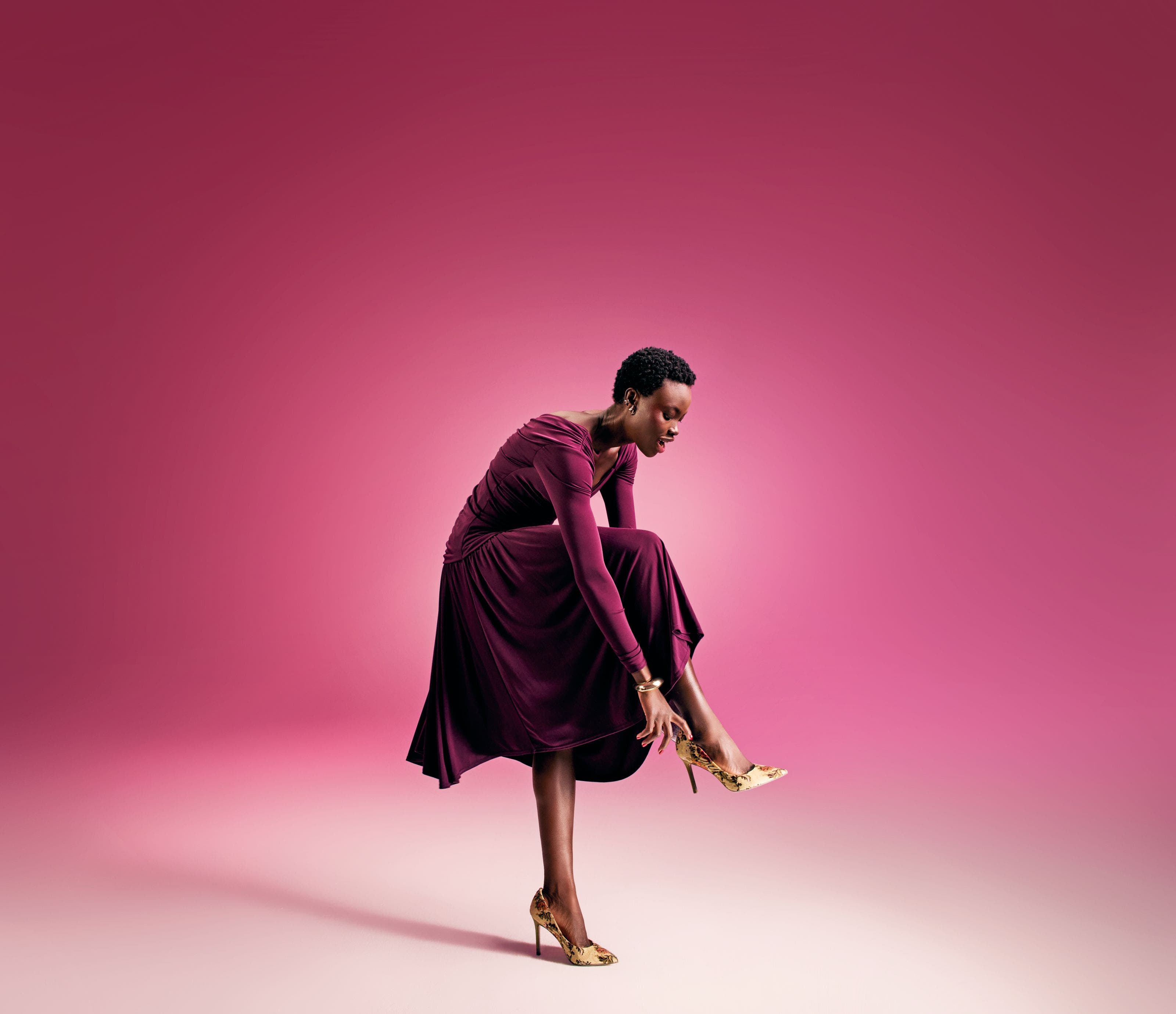 A woman wearing a burgundy dress and gold heels.