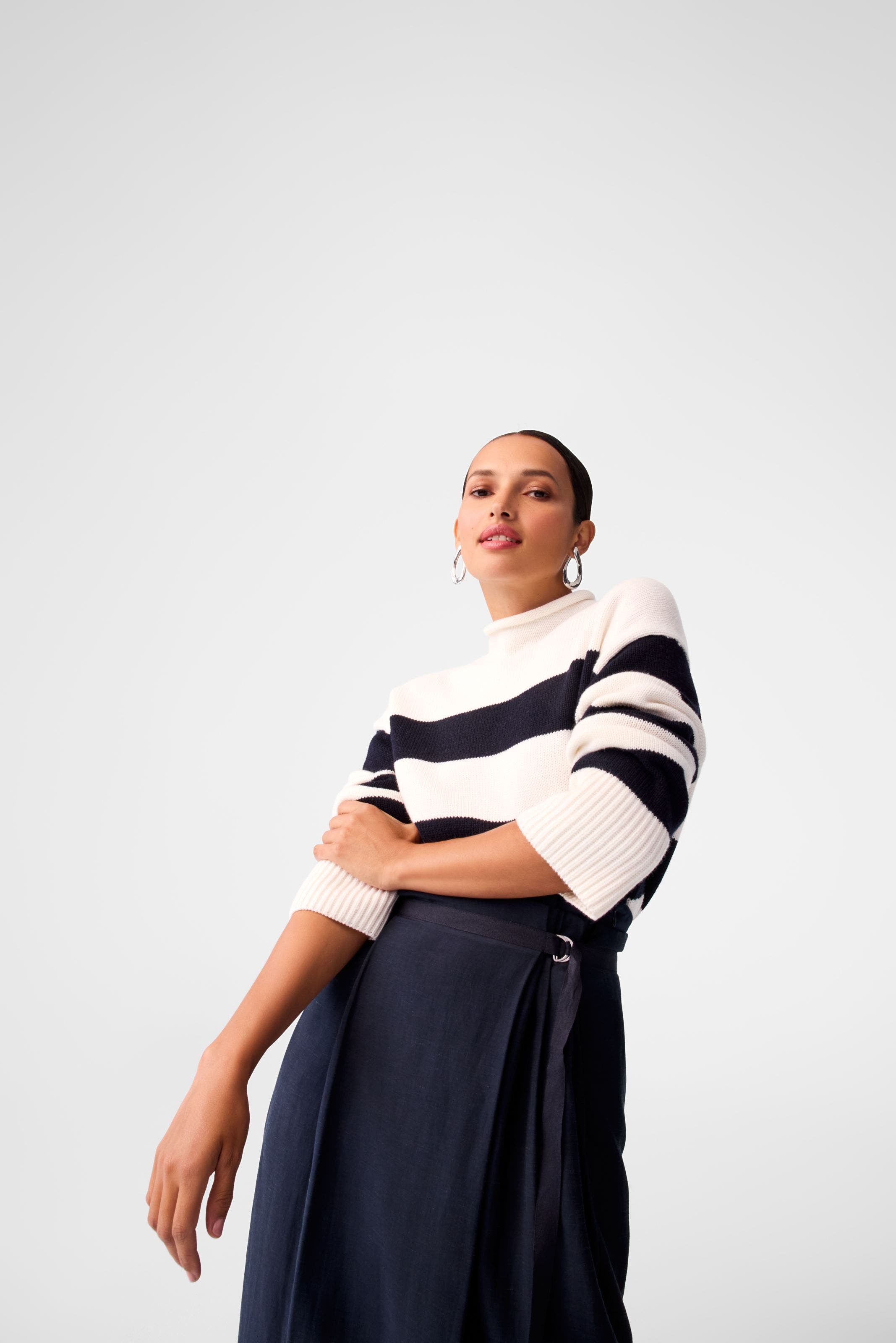 A woman wearing a striped sweater and navy skirt.