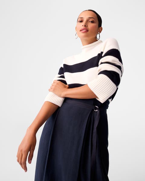 A woman wearing a striped sweater and navy skirt.