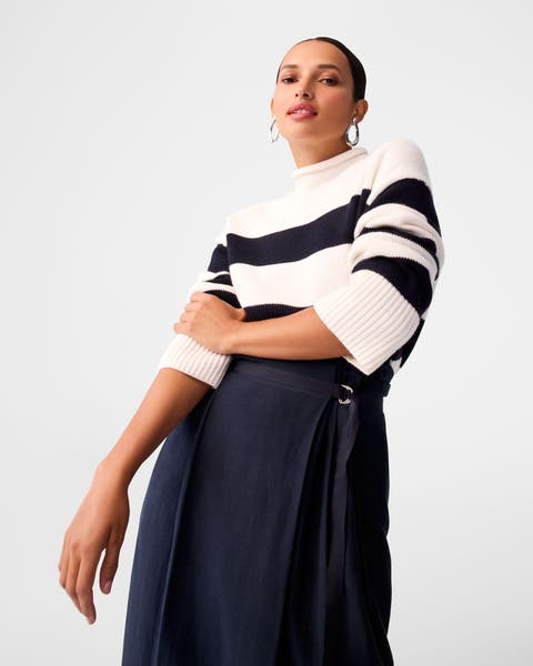 A woman wearing a striped sweater and navy skirt.