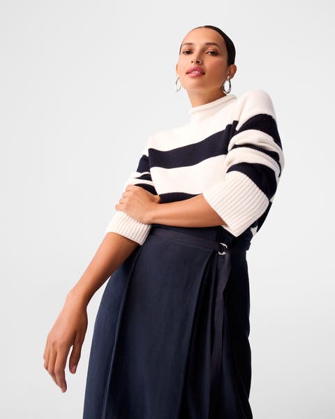 A woman wearing a striped sweater and navy skirt.