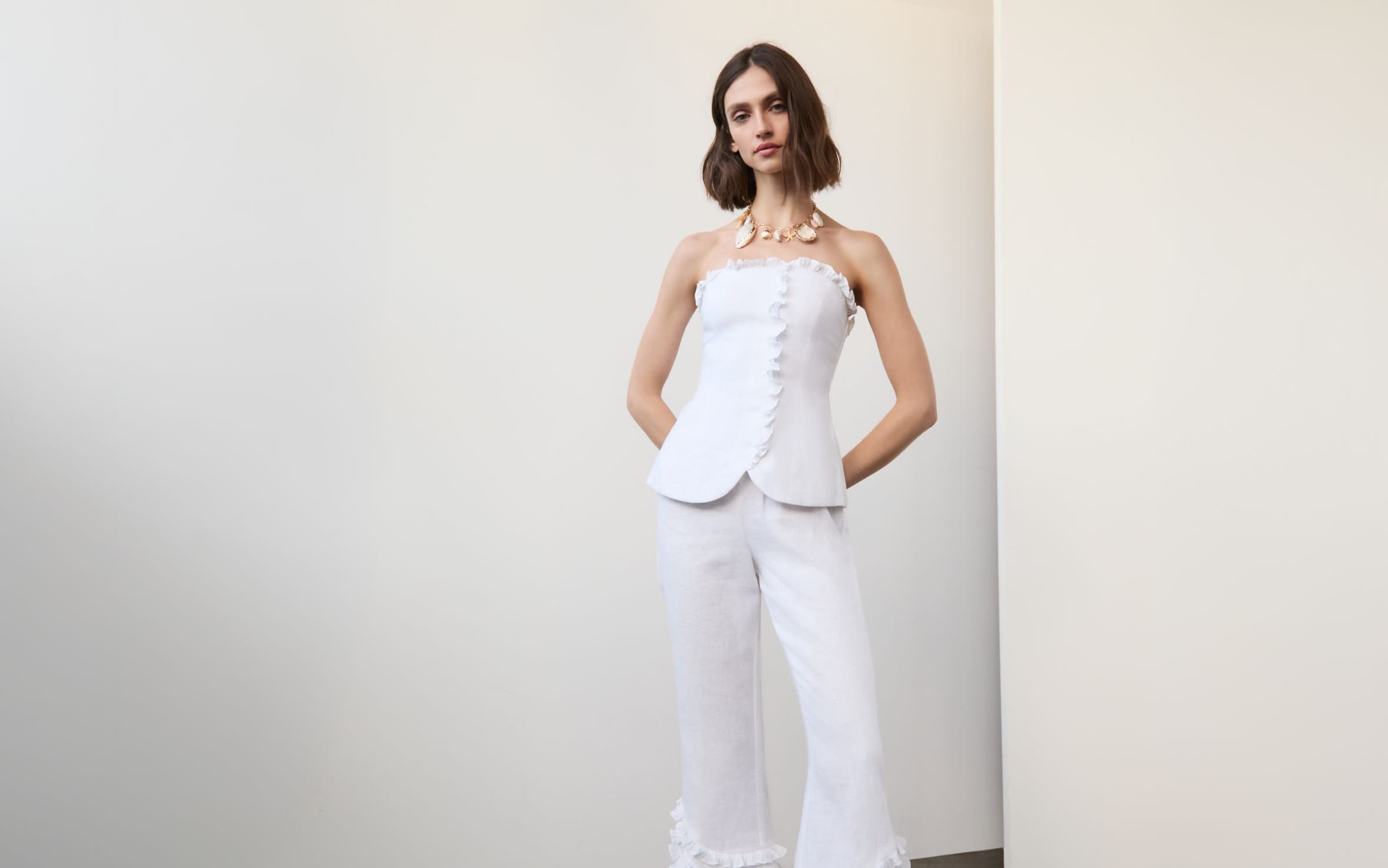 Woman wearing a white linen matching set with a statement necklace and flip-flop heels.