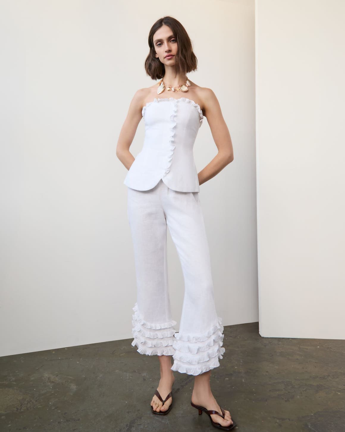 Woman wearing a white linen matching set with a statement necklace and flip-flop heels.