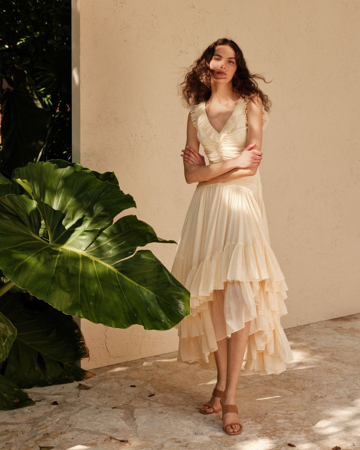 Woman wearing a Cinq a Sept dress standing in front of a wall and elephant ear plant.