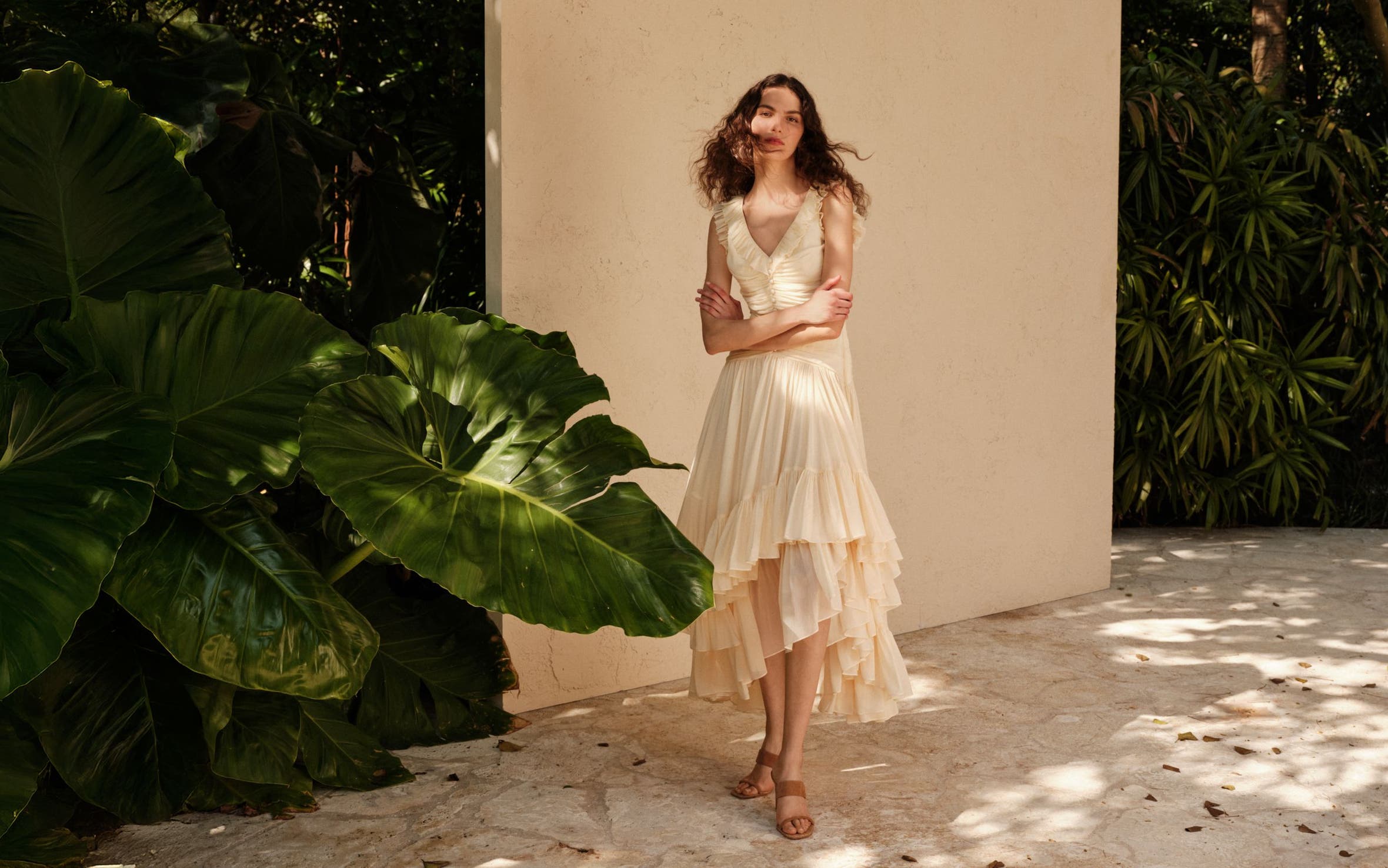 Woman wearing a Cinq a Sept dress standing in front of a wall and elephant ear plant.