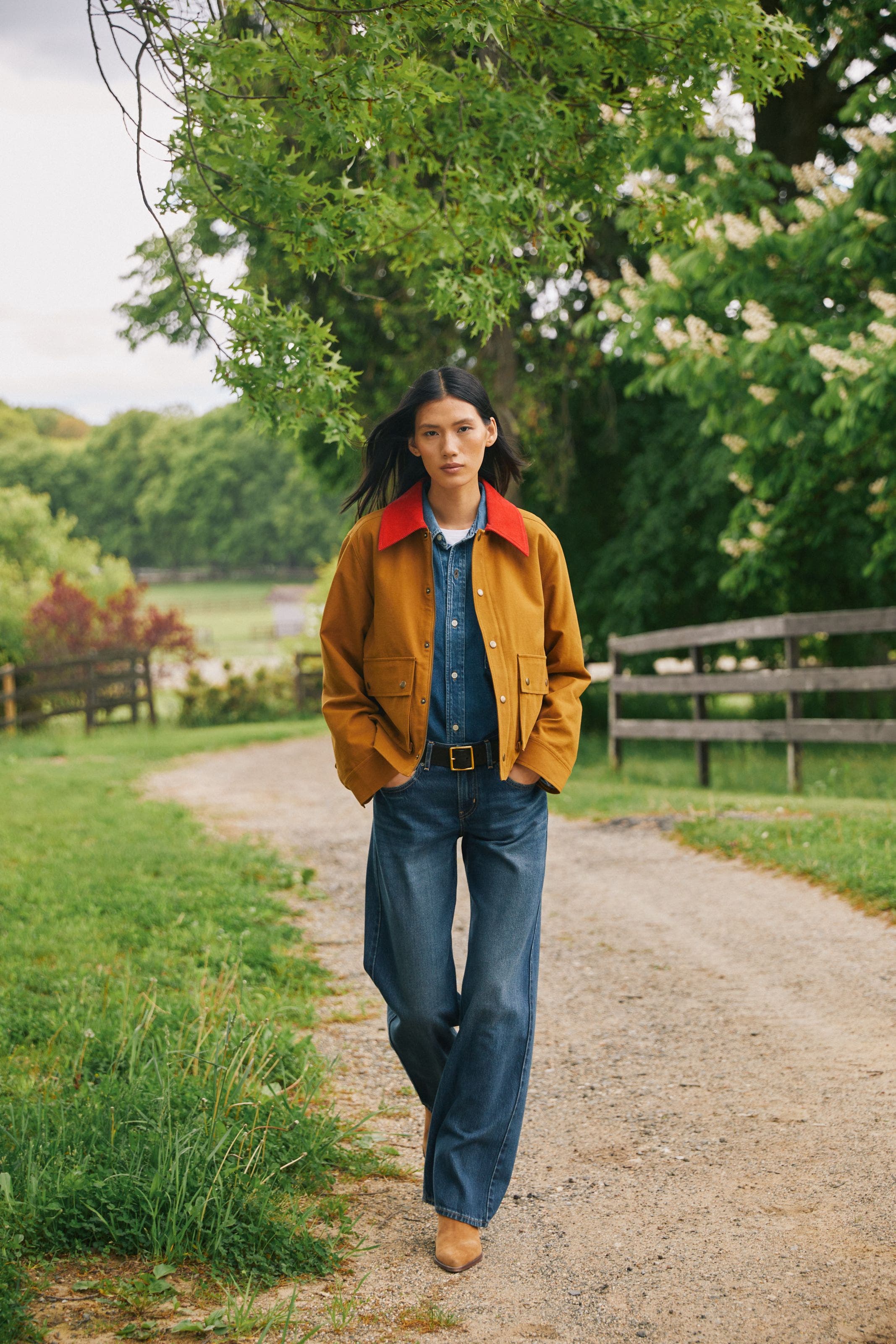 A woman wearing a denim button up and denim jeans with a brown chore jacket.