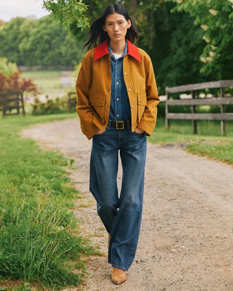 A woman wearing a denim button up and denim jeans with a brown chore jacket.