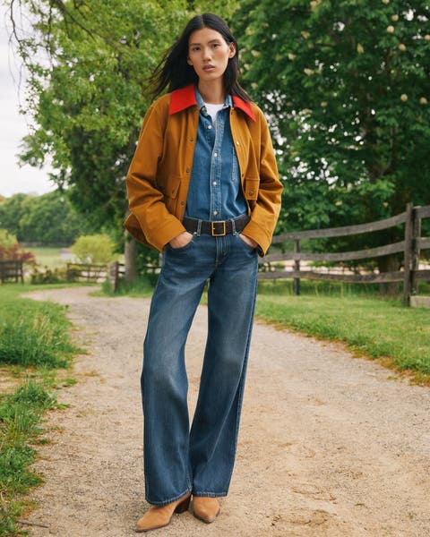Woman in a denim button-down and jeans with an orange canvas jacket on top.