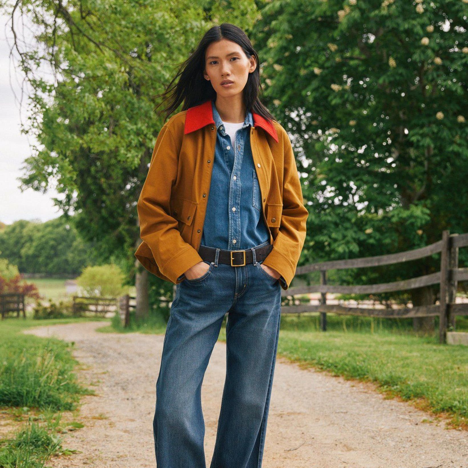 A woman wearing a denim shirt and jeans layered with a mustard-colored jacket.