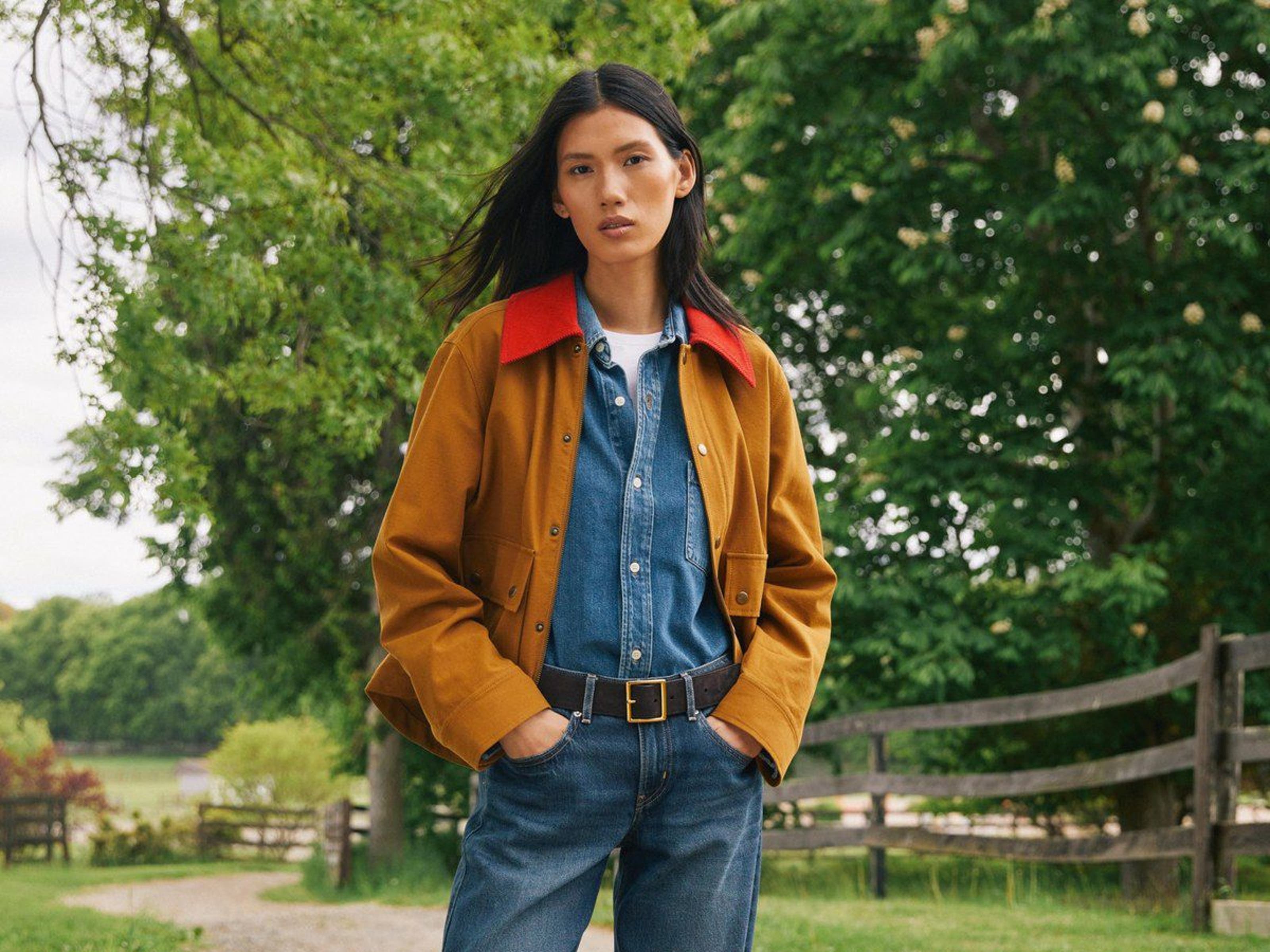 A woman wearing a denim shirt and jeans layered with a mustard-colored jacket.