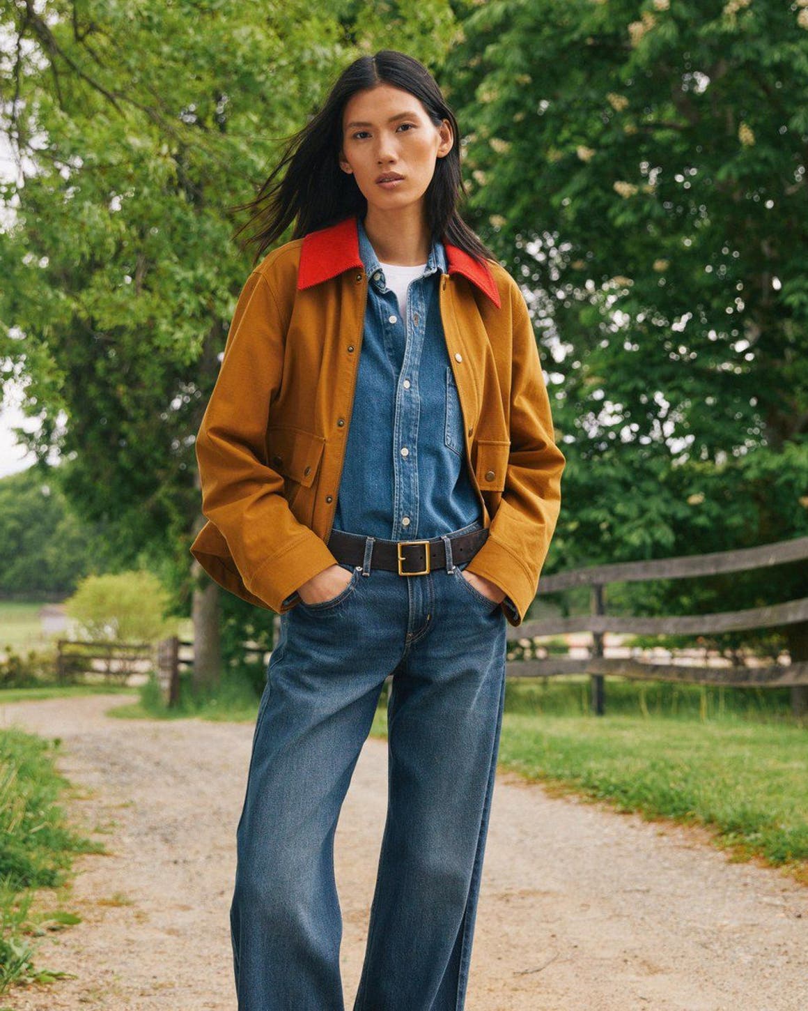 A woman wearing a denim shirt and jeans layered with a mustard-colored jacket.