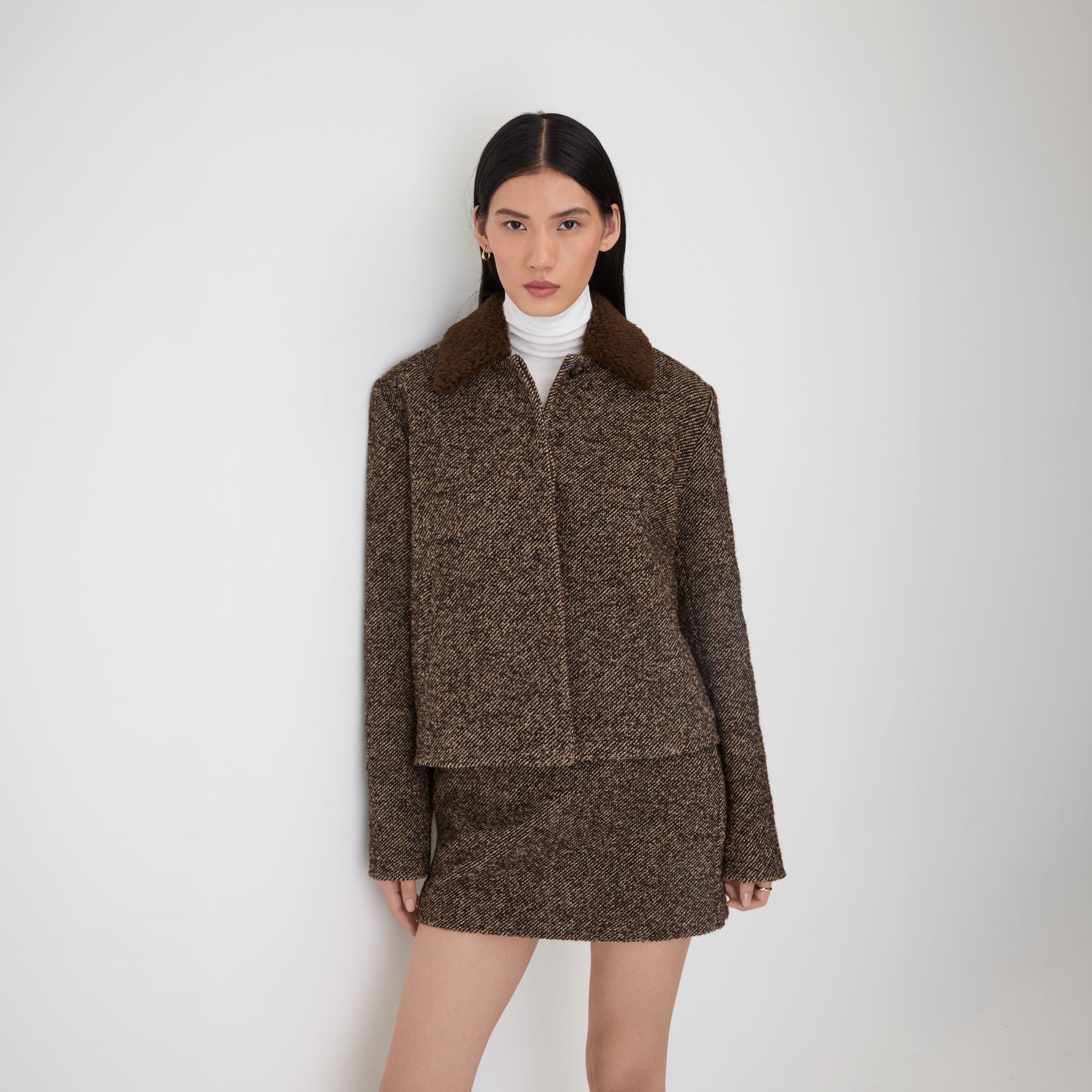 A woman wearing a brown wool jacket and matching mini skirt.