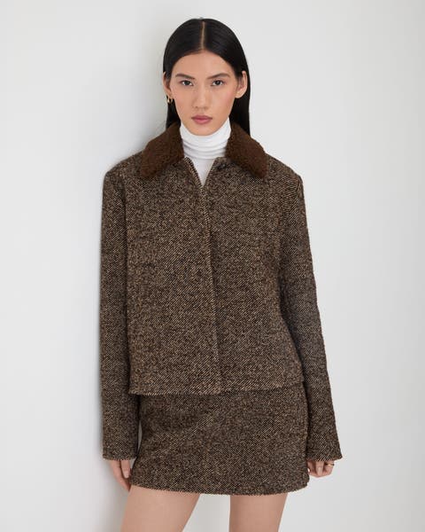 A woman wearing a brown wool jacket and matching mini skirt.