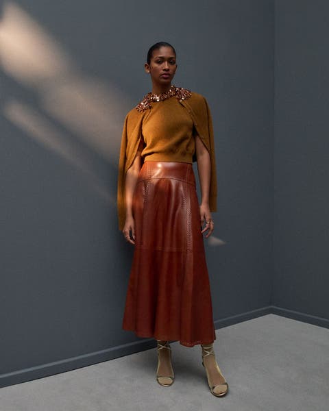 Woman wearing an embellished sweater set, leather skirt and heels.