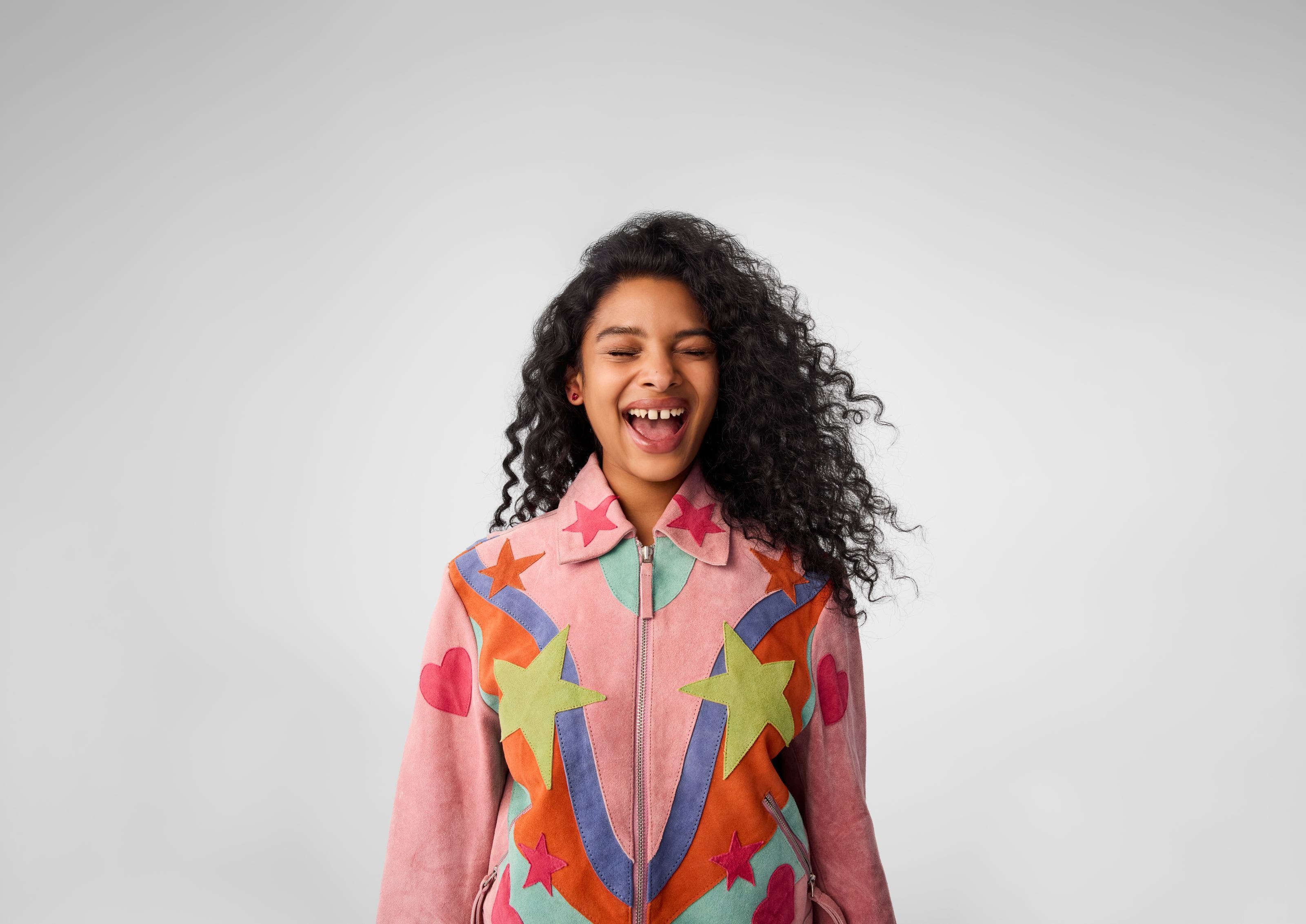A young woman wearing a pink jacket with colorful stars and hearts on it.