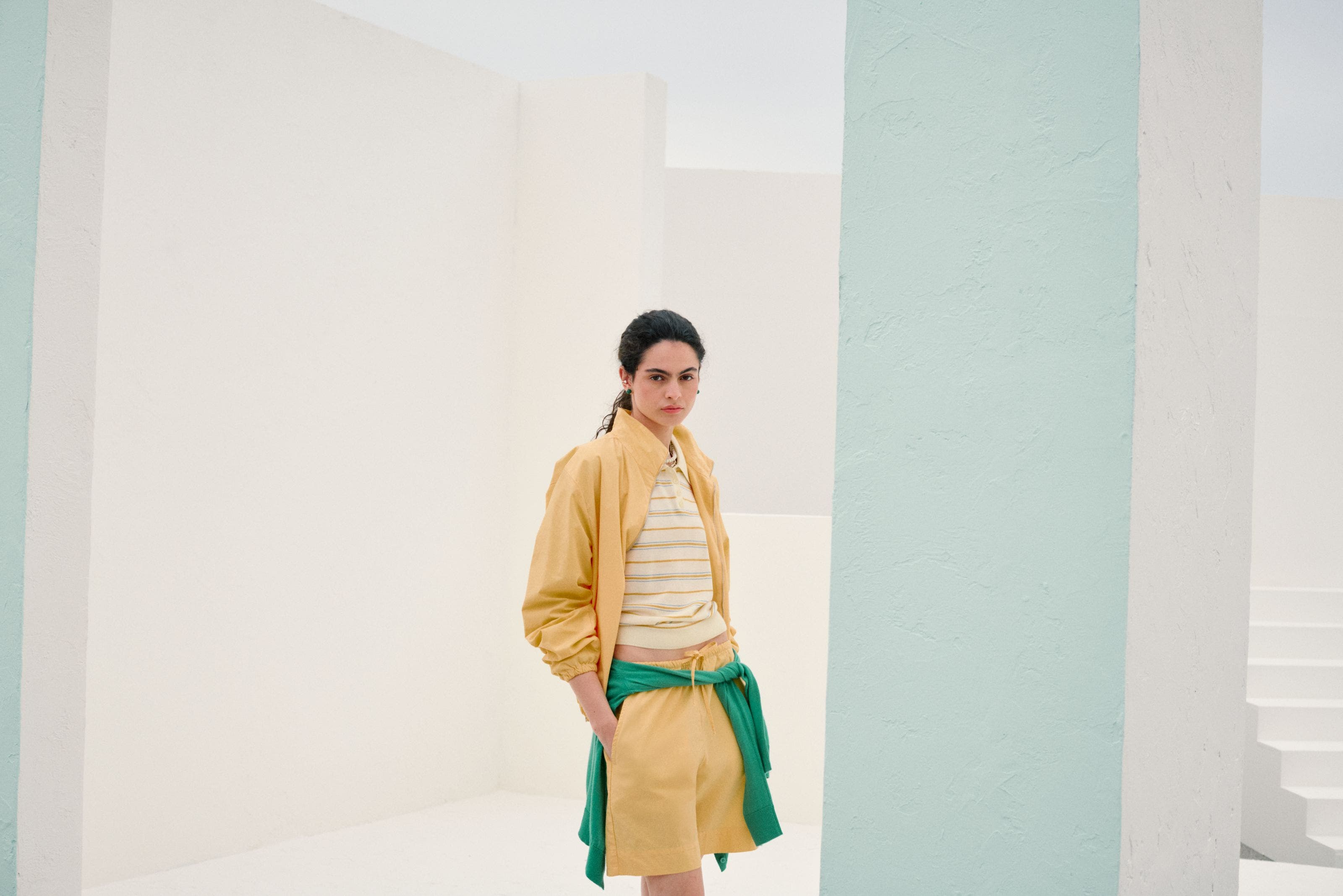 Woman wearing a yellow matching set with a striped polo and a green sweatshirt tied at the waist.