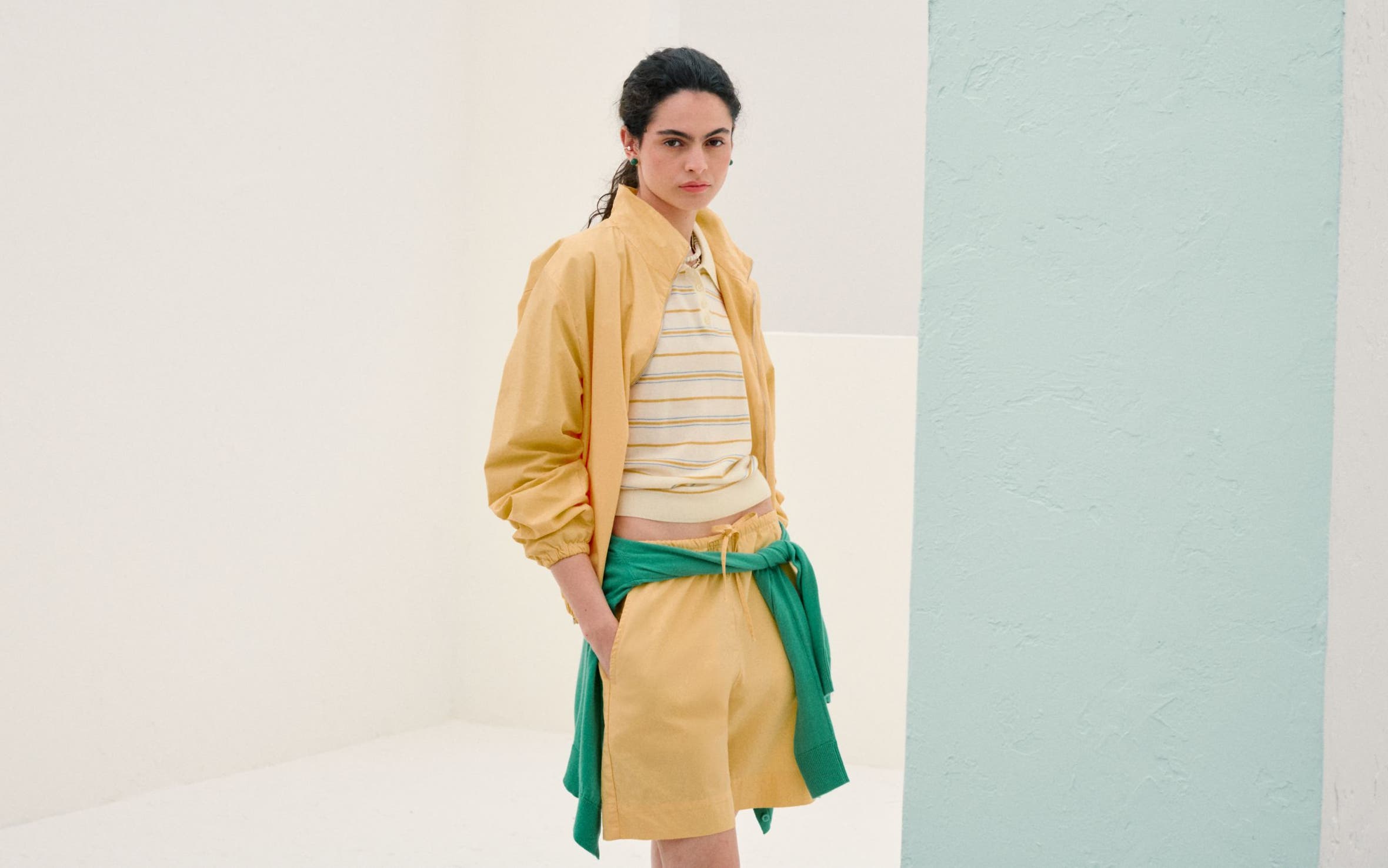 Woman wearing a yellow matching set with a striped polo and a green sweatshirt tied at the waist.