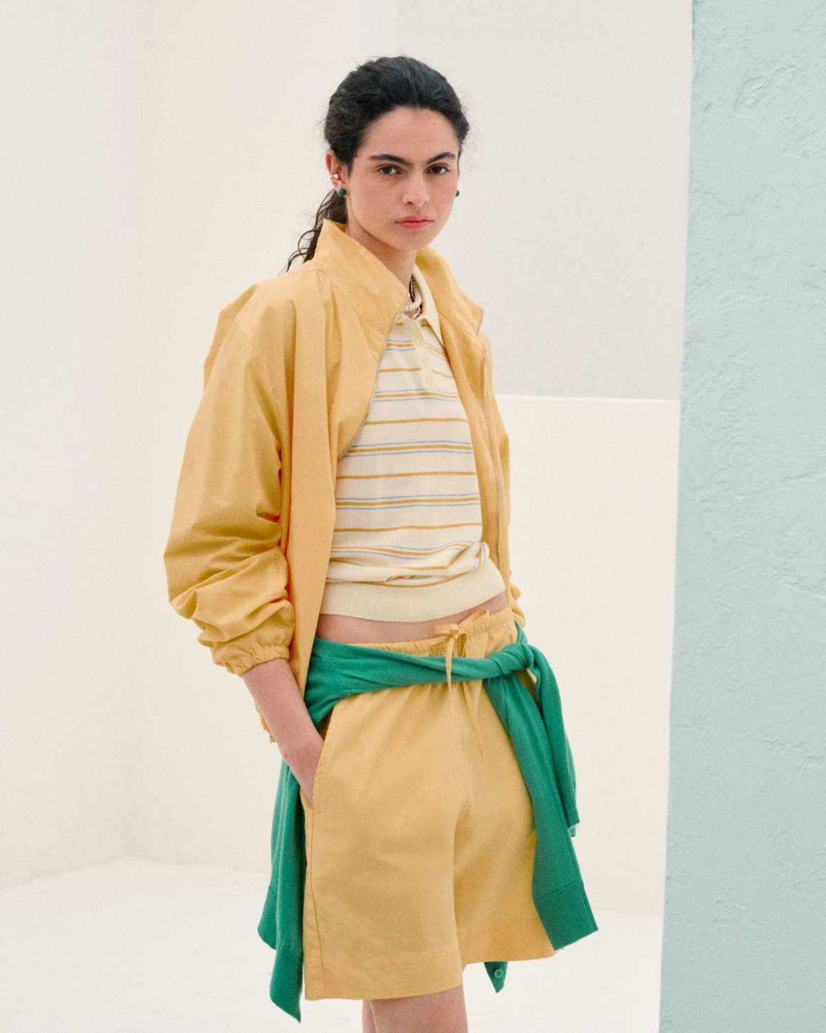 Woman wearing a yellow matching set with a striped polo and a green sweatshirt tied at the waist.