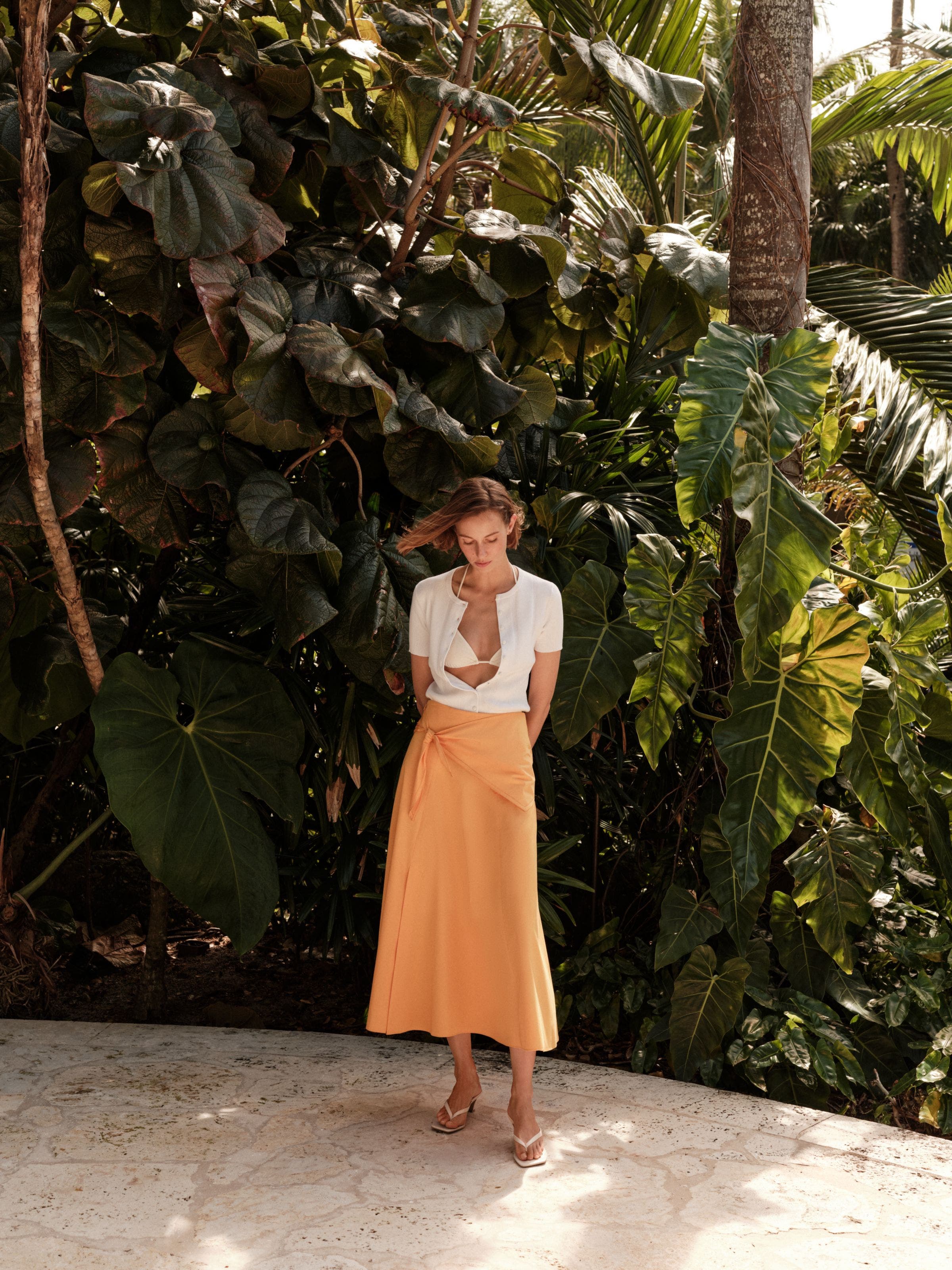 Woman wearing a cardigan, bikini top, wrap maxi skirt and flip-flop heels.
