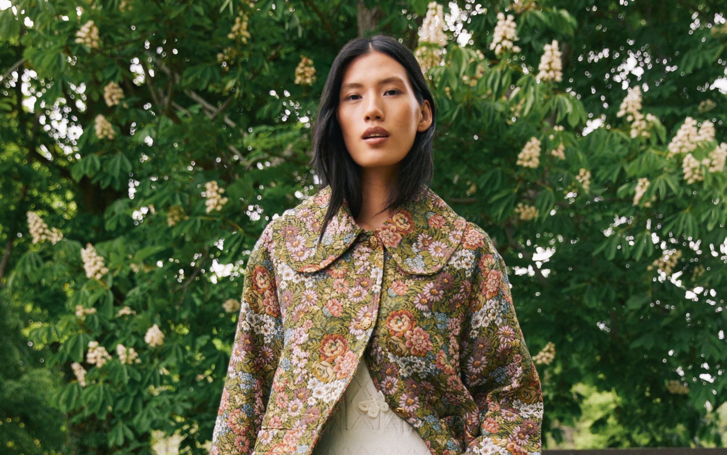 A woman wearing a floral jacket and skirt.