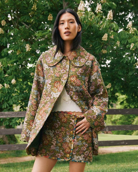 A woman wearing a floral print jacket and matching skirt.