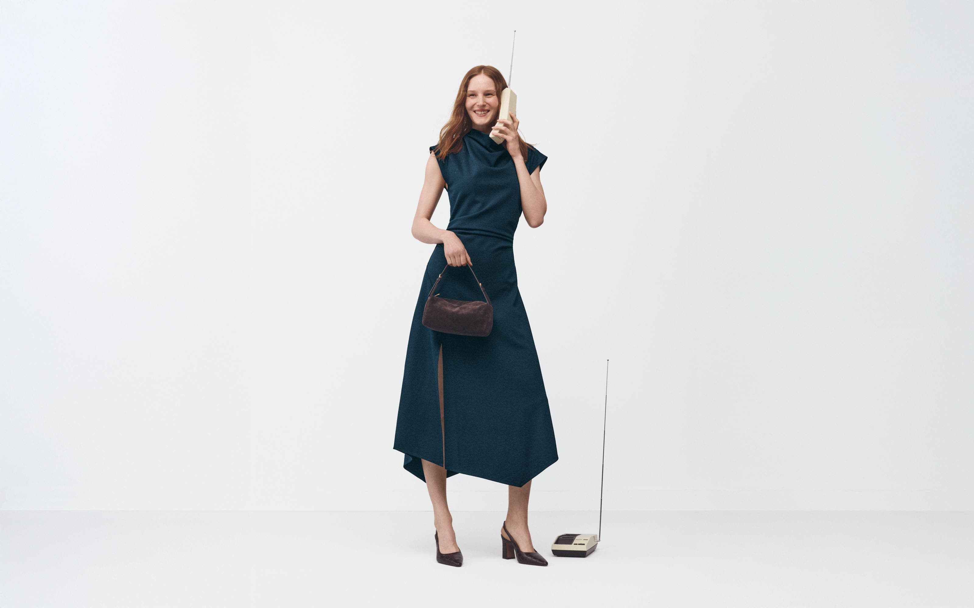 A woman wearing a dress and heels holding a handbag.