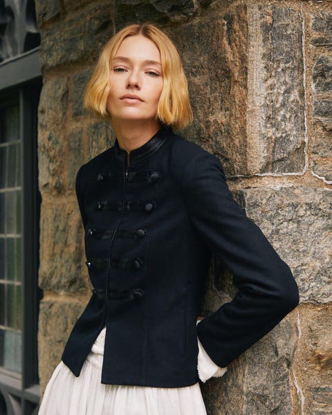 A woman in a navy military-style jacket, ivory ruffled skirt.