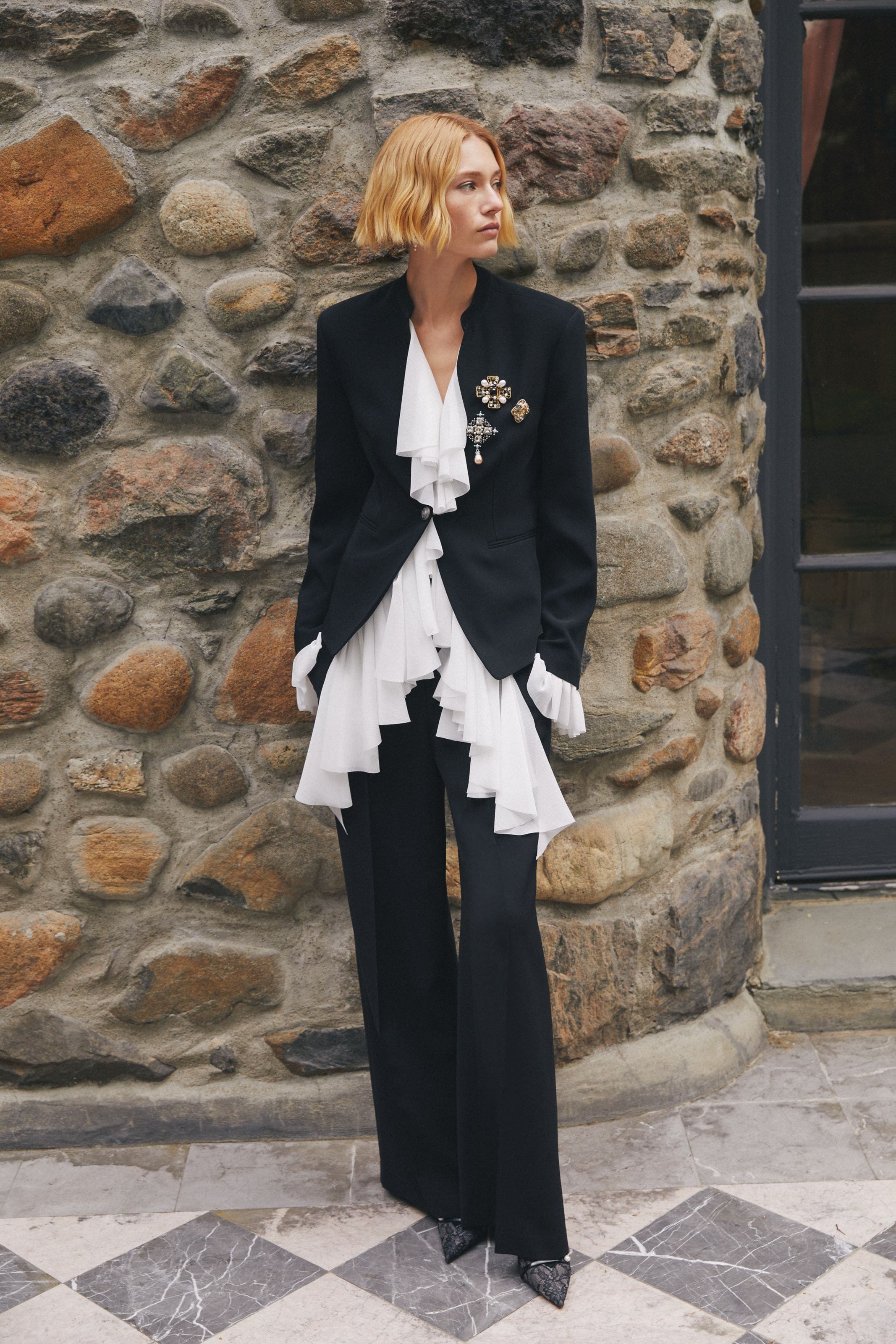 A woman wearing a black blazer with a white ruffled blouse.
