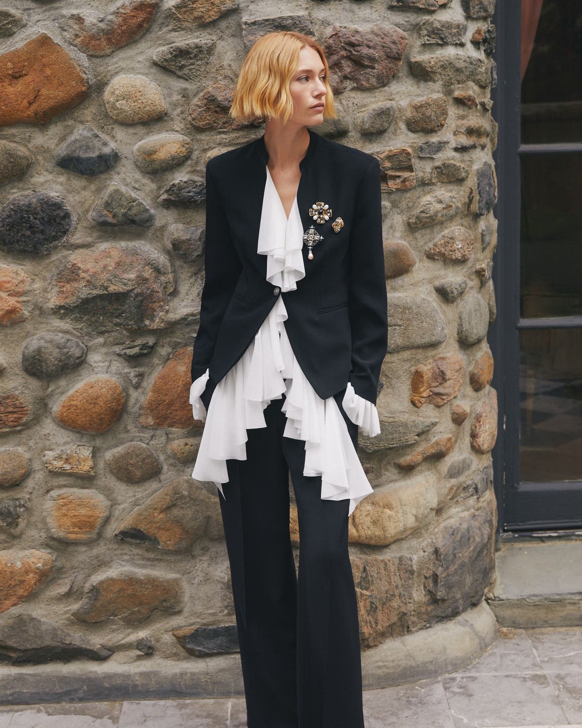 A woman wearing a black blazer with a white ruffled blouse.
