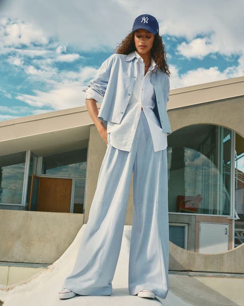 A woman wearing matching blue cropped jacket and pants over a white button down, a Yankee's baseball hat.