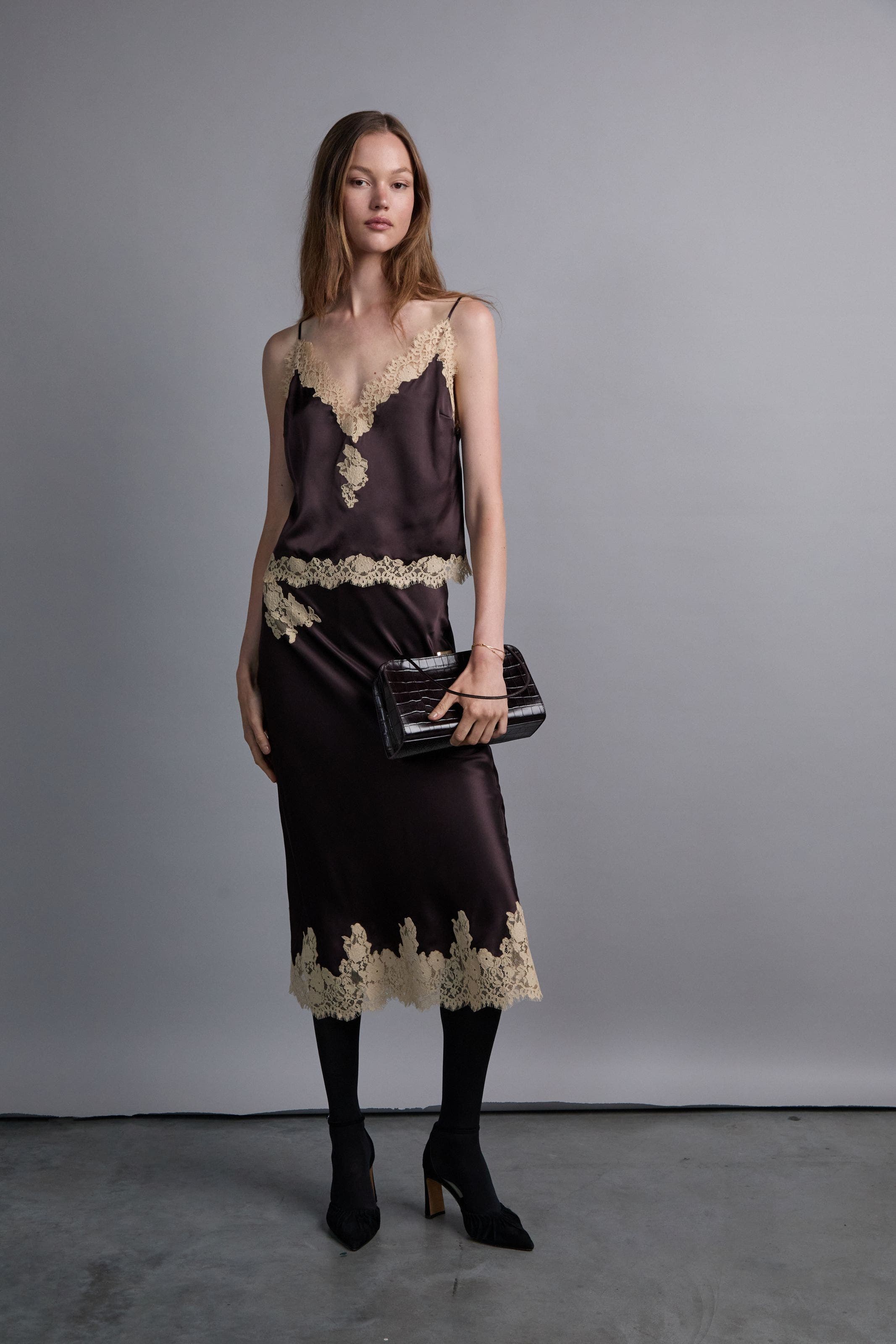 A woman wearing a brown lace-trimmed satin top and matching satin skirt.