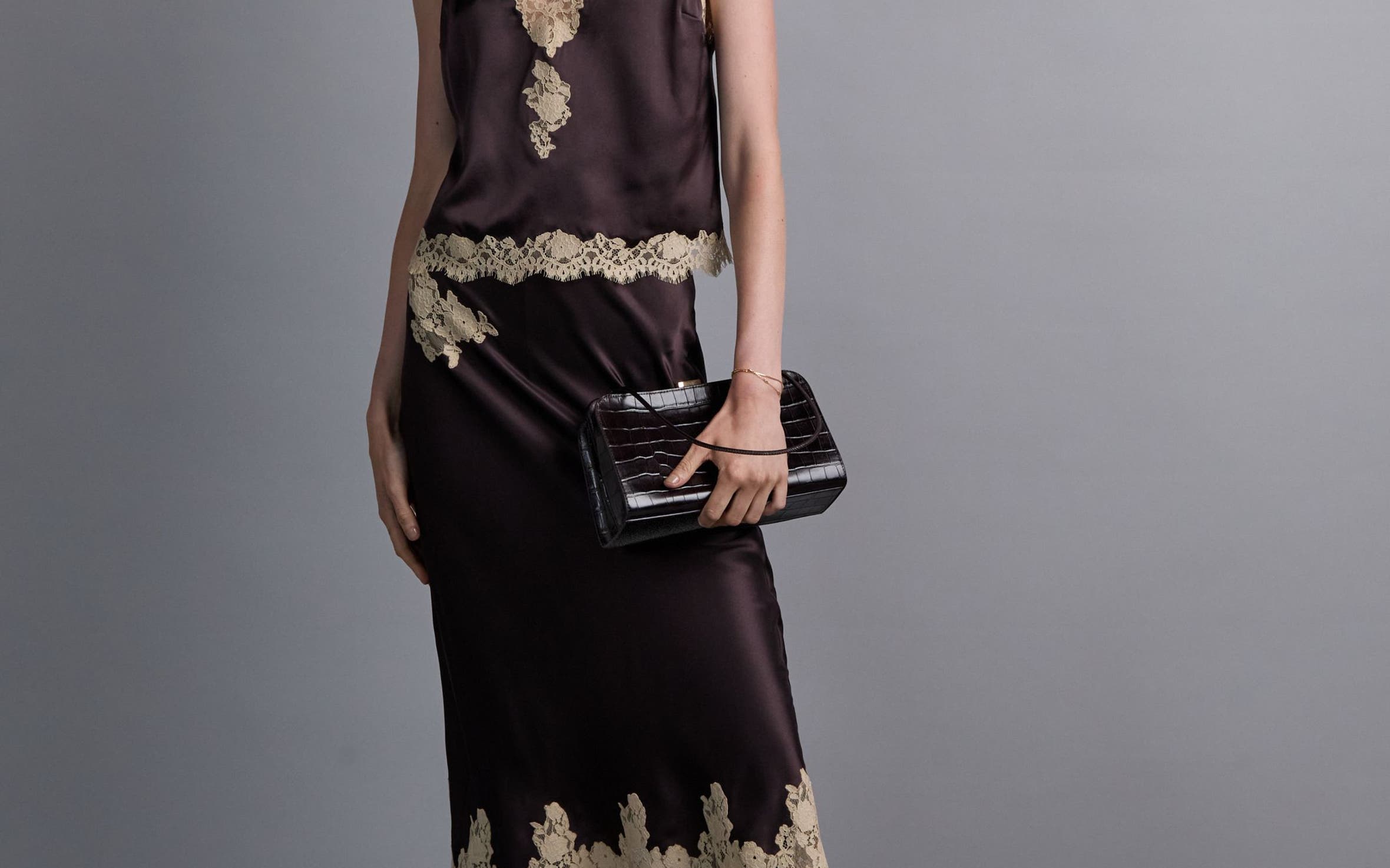 A woman wearing a brown lace-trimmed satin top and matching satin skirt.