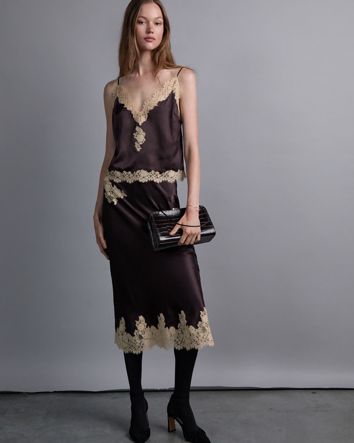 A woman wearing a brown lace-trimmed satin top and matching satin skirt.