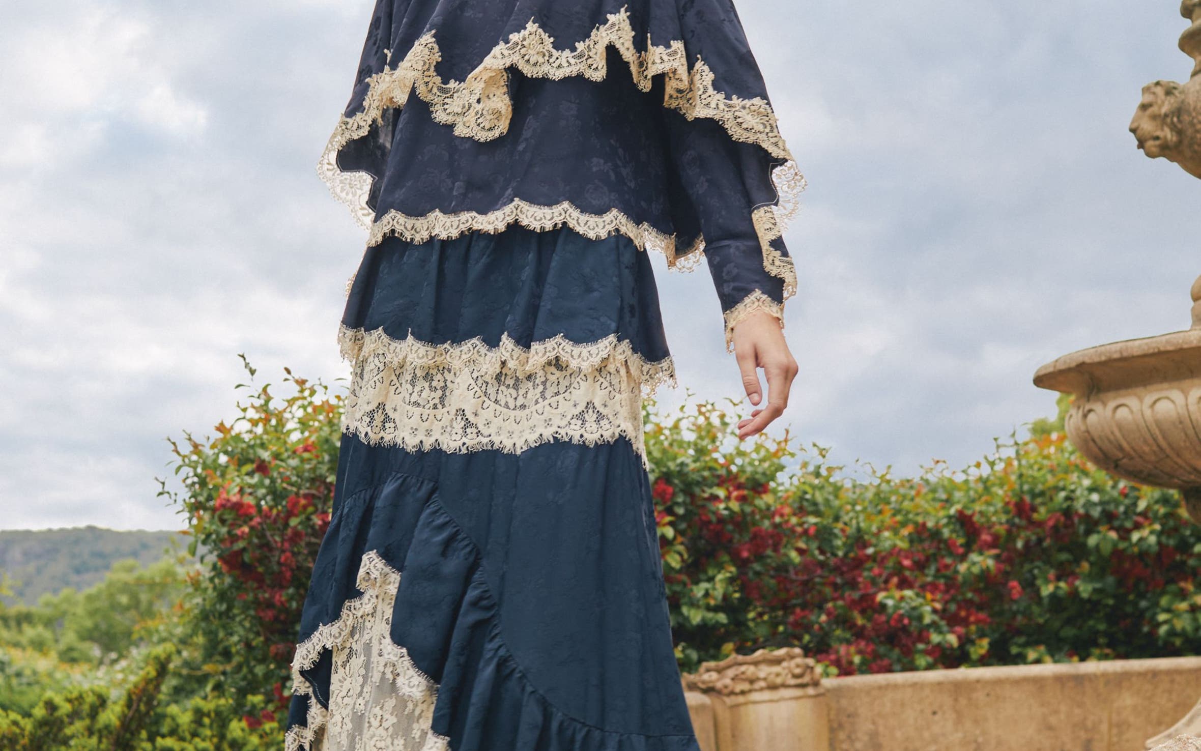 A woman wearing a long tiered navy and cream lace dress.