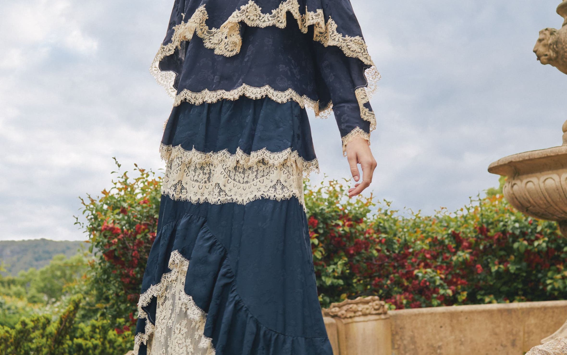 A woman wearing a long tiered navy and cream lace dress.