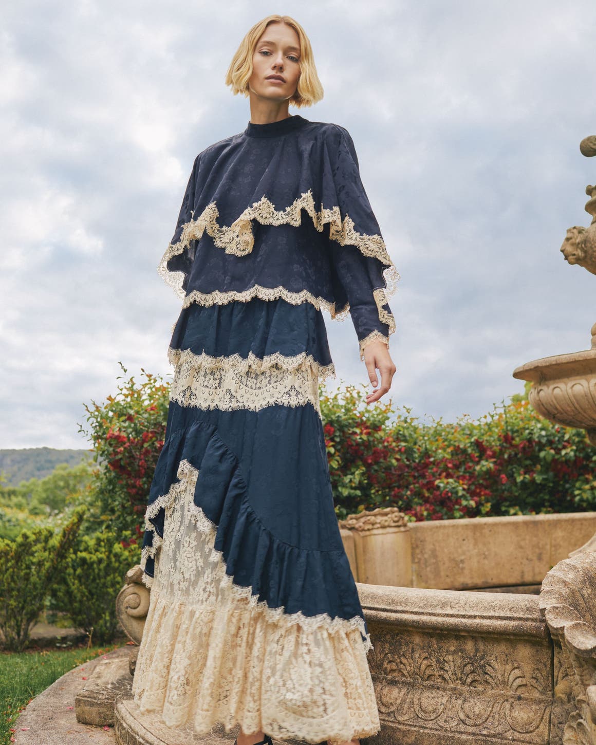 A woman wearing a long tiered navy and cream lace dress.