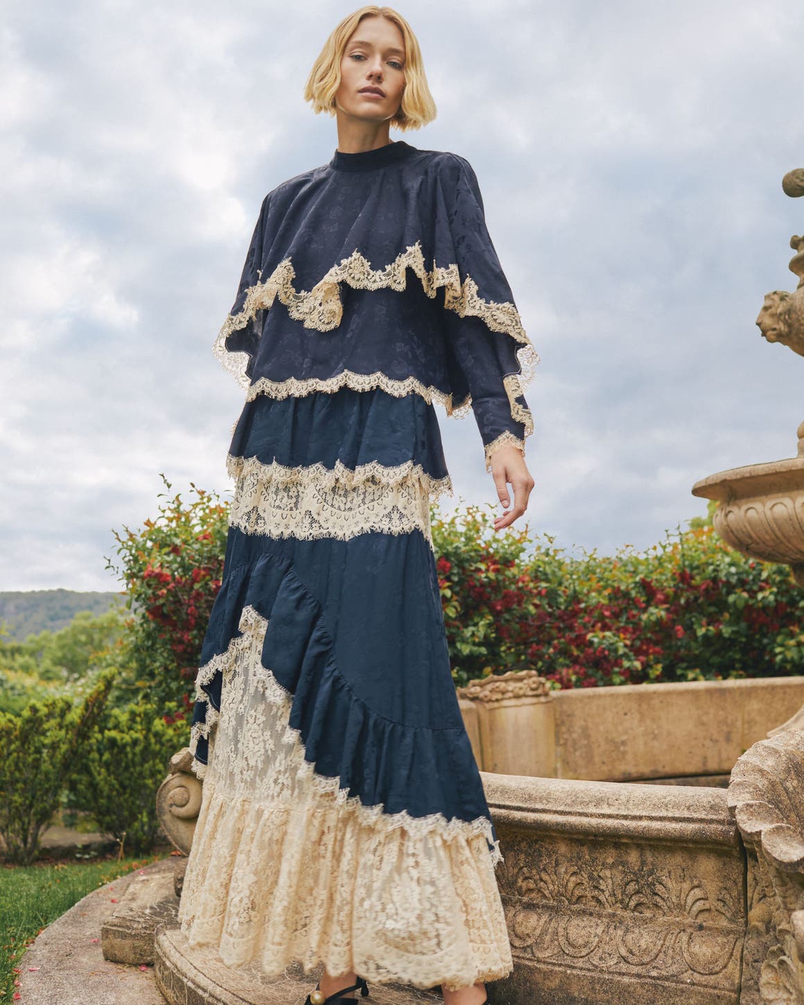 A woman wearing a long tiered navy and cream lace dress.
