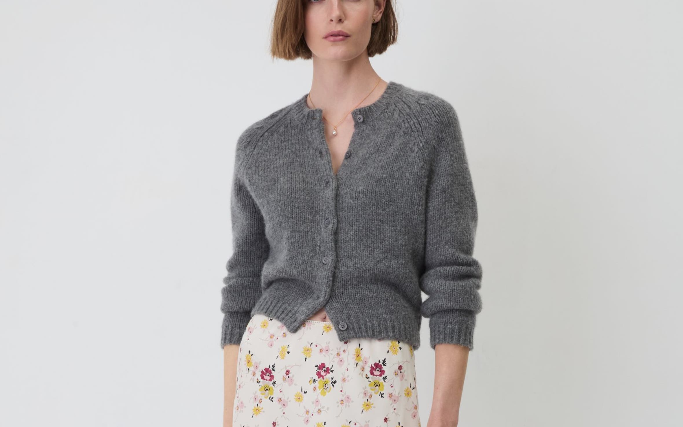 A woman wearing a grey cardigan and floral skirt.