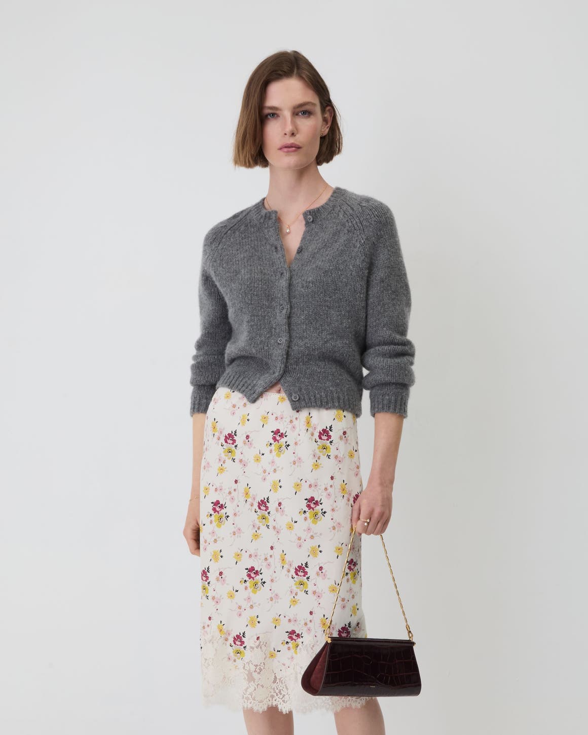 A woman wearing a grey cardigan and floral skirt.
