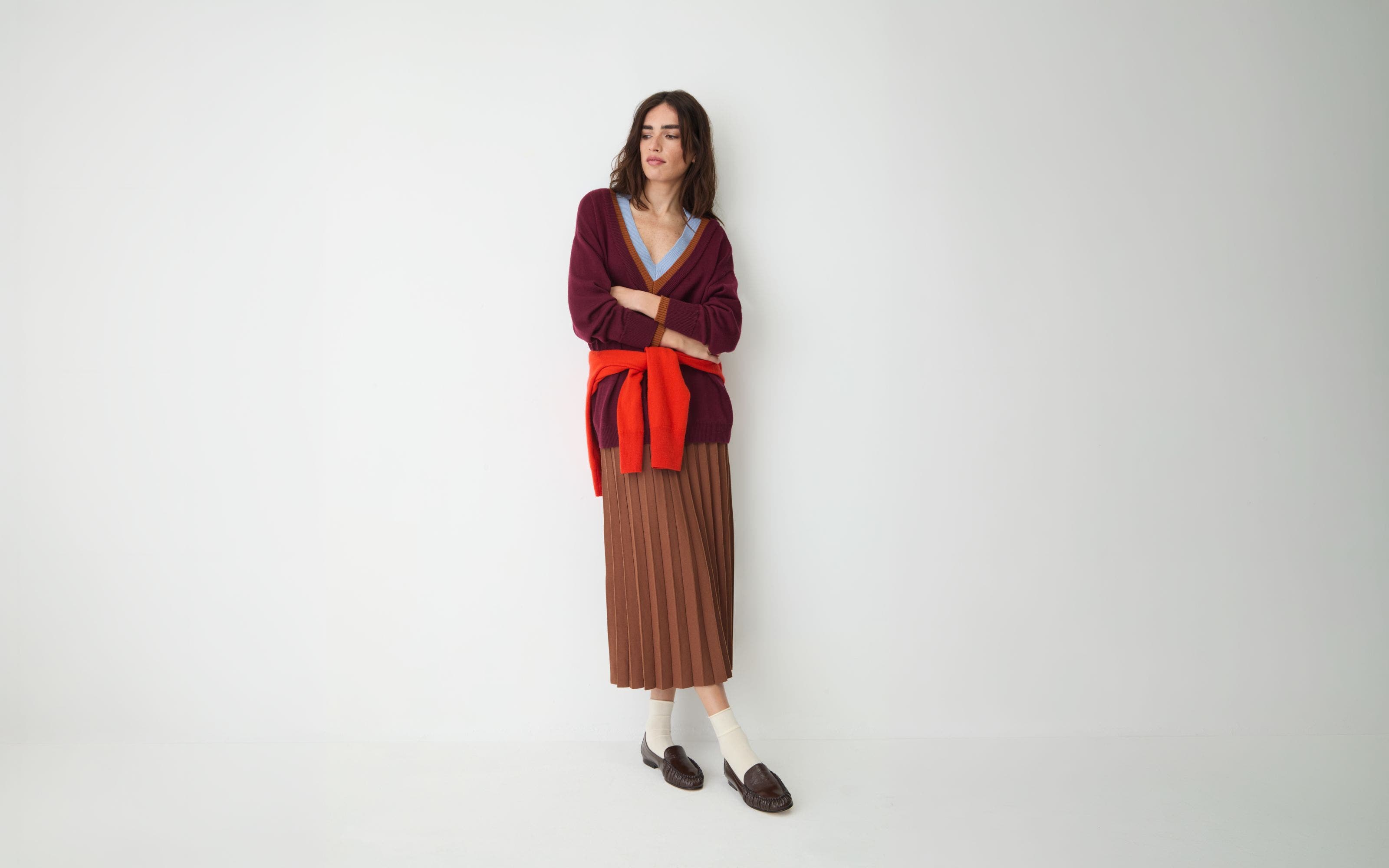 Woman in pleated skirt and layered knitwear.