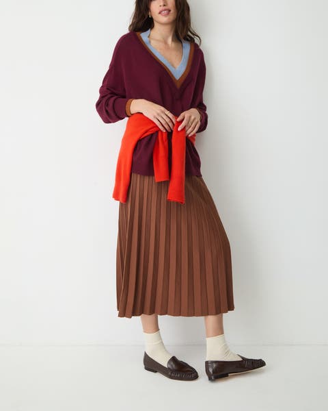 A woman wearing brown leather penny loafers and a pleated midi skirt.