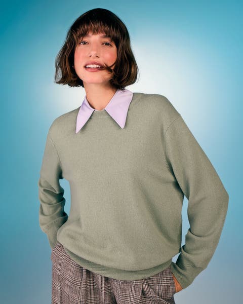 Woman wearing a light sage green sweater over a lavender pointed-collar shirt, paired with plaid trousers.