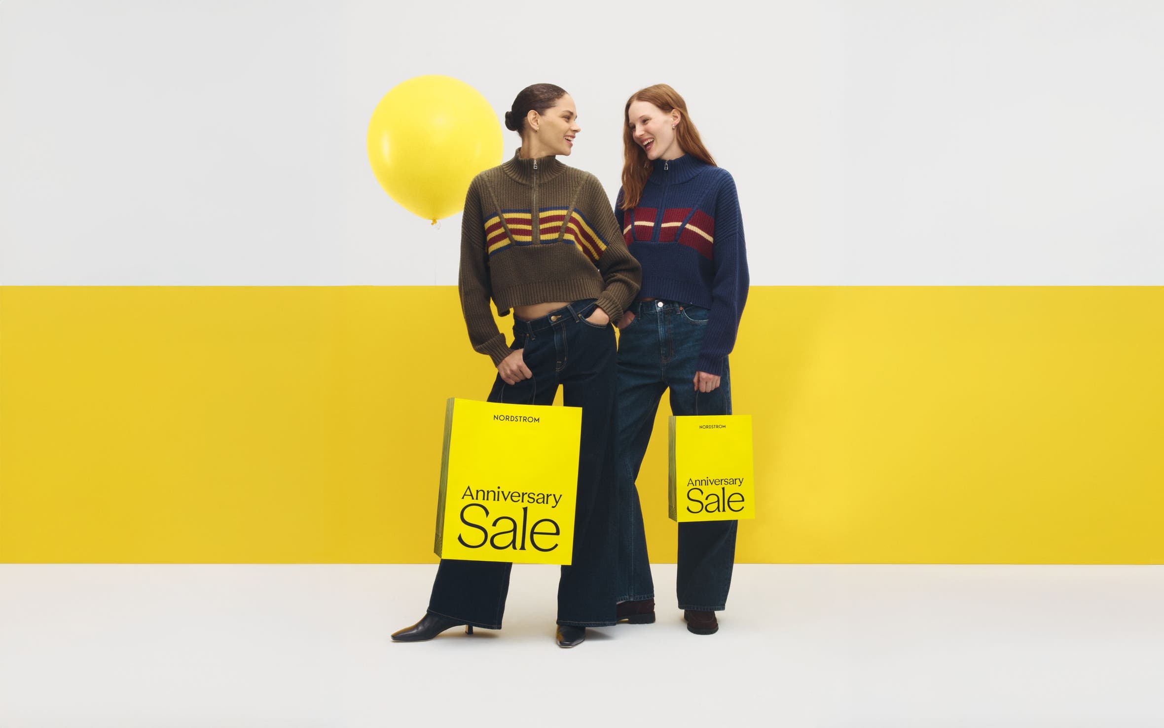 Two women in wide-leg pants and striped zip-ups, carrying Anniversary Sale bags.