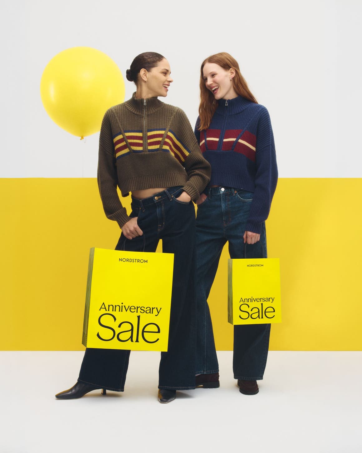 Two women in wide-leg pants and striped zip-ups, carrying Anniversary Sale bags.