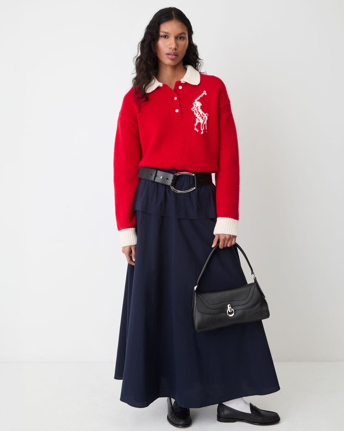 A woman wearing a red crewneck sweater and black maxi skirt.