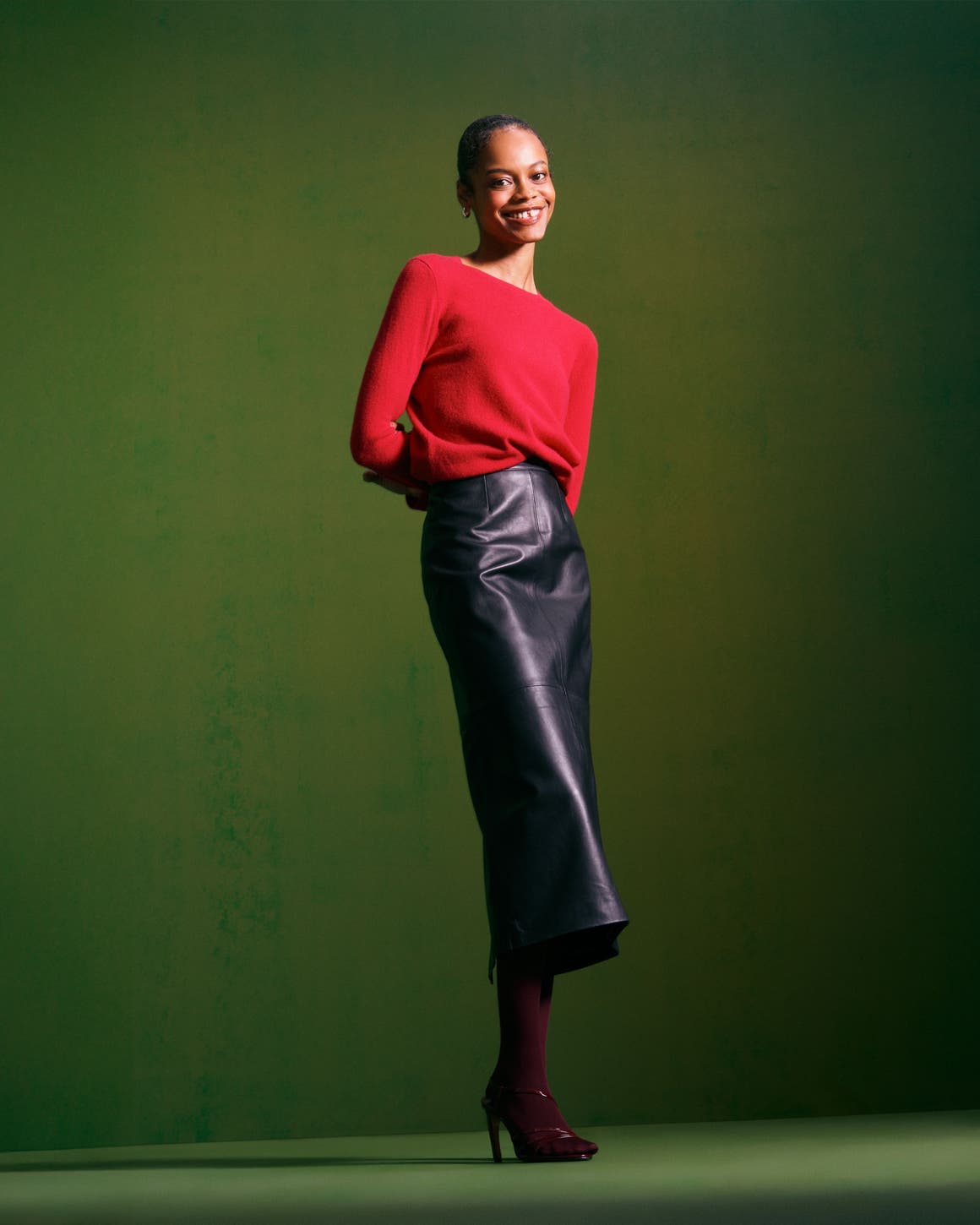 Woman wearing a cashmere sweater, leather skirt, tights, heels and a handbag.