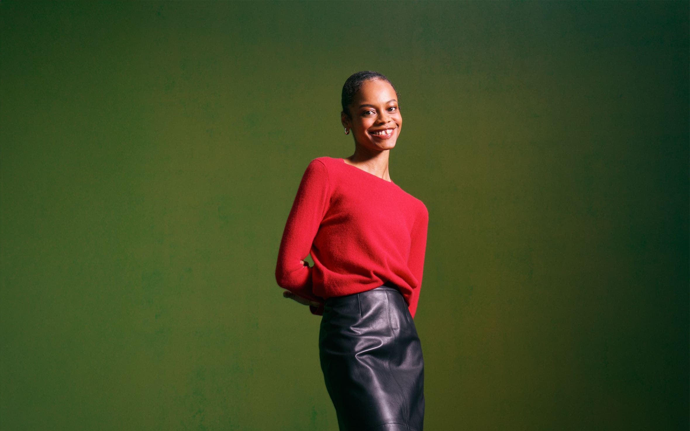 Woman wearing a cashmere sweater, leather skirt, tights, heels and a handbag.