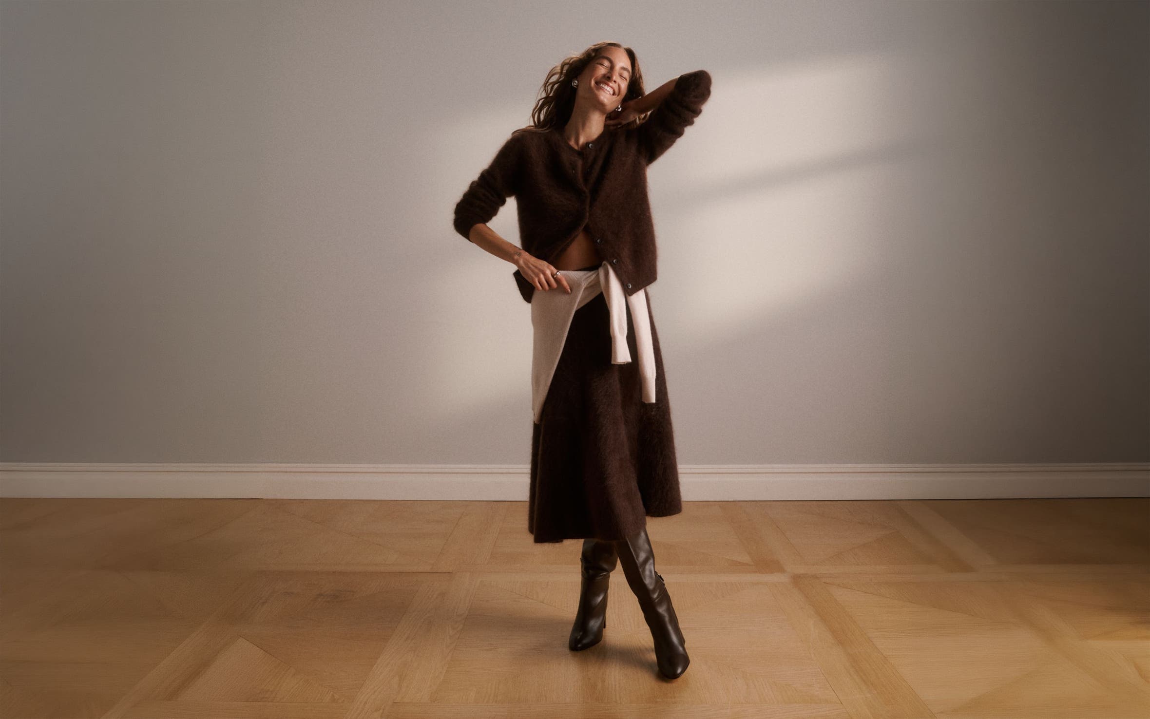 A woman wearing a cardigan and skirt with a sweater around her waist.