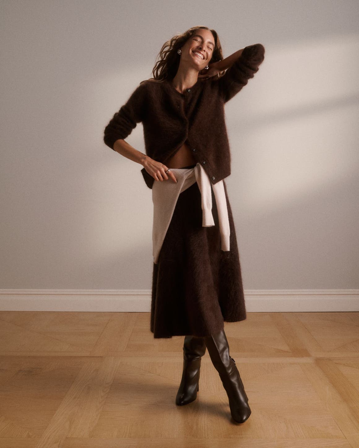 A woman wearing a cardigan and skirt with a sweater around her waist.
