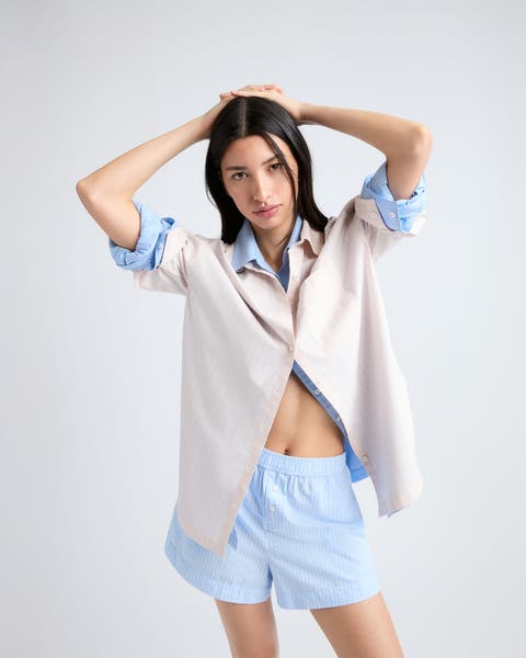 Woman wearing two layered button-up shirts and boxer shorts.
